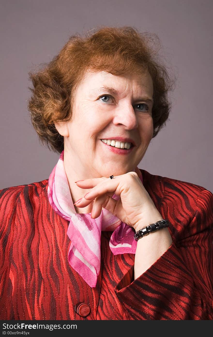 The cheerful elderly woman in a red dress on a grey background. The cheerful elderly woman in a red dress on a grey background.