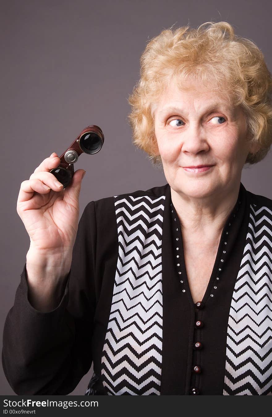 The cheerful elderly woman with binocular on a grey background. The cheerful elderly woman with binocular on a grey background.