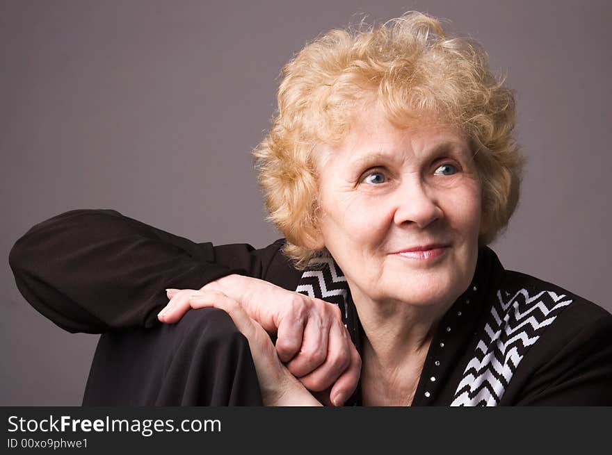 The elderly woman in a black dress on a grey background. The elderly woman in a black dress on a grey background.