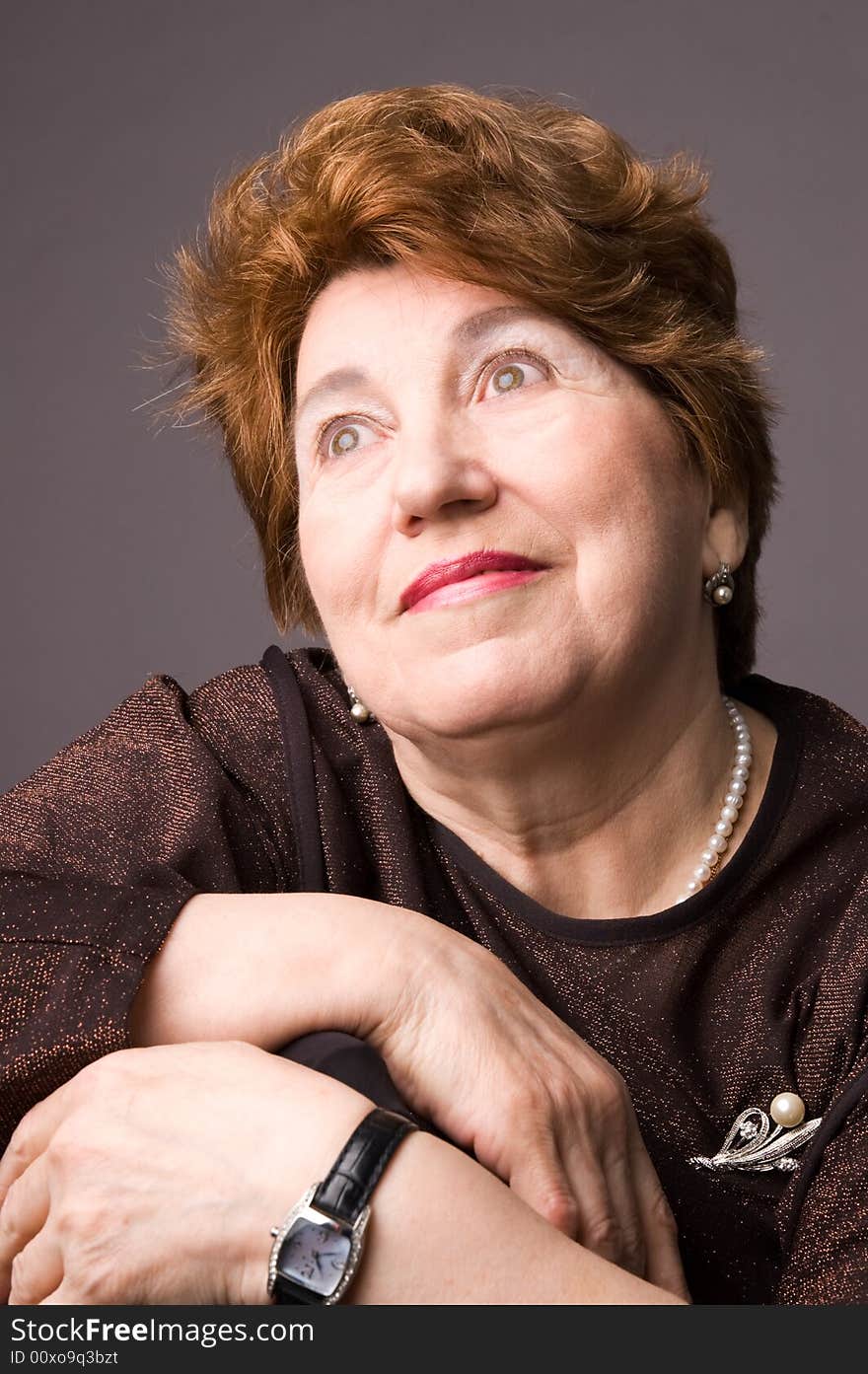 The cheerful elderly woman in a brown dress on a grey background. The cheerful elderly woman in a brown dress on a grey background.