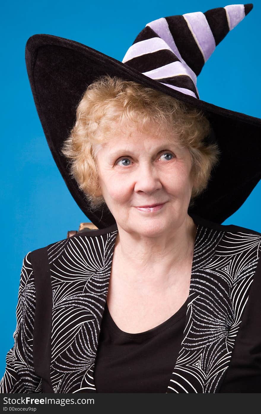 The cheerful elderly woman in witch's hat on a blue background. The cheerful elderly woman in witch's hat on a blue background.