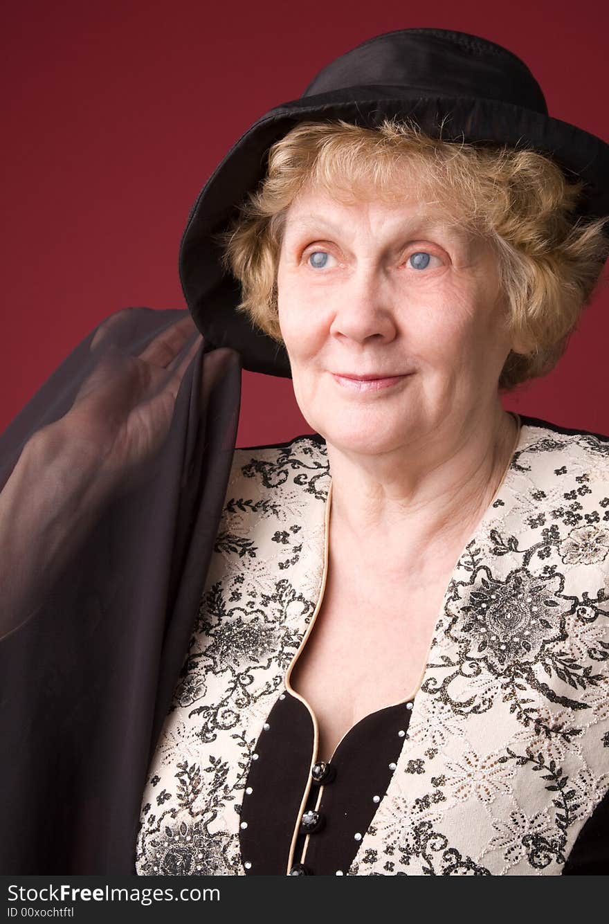 The cheerful elderly woman in hat on a red background. The cheerful elderly woman in hat on a red background.