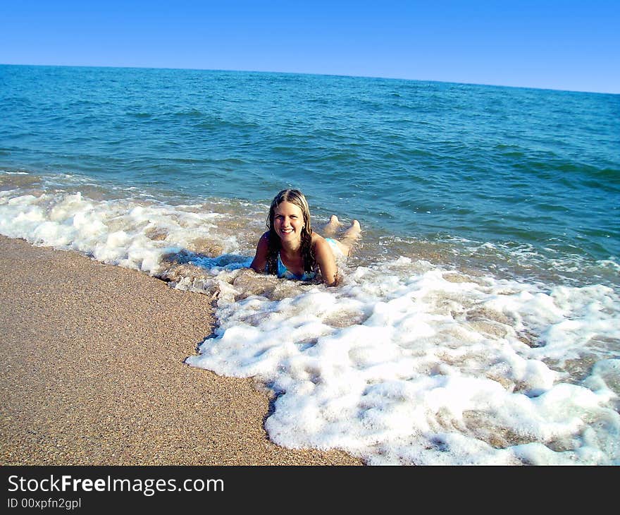 The lying girl on sand enjoys waves of a surf in the sea. The lying girl on sand enjoys waves of a surf in the sea.