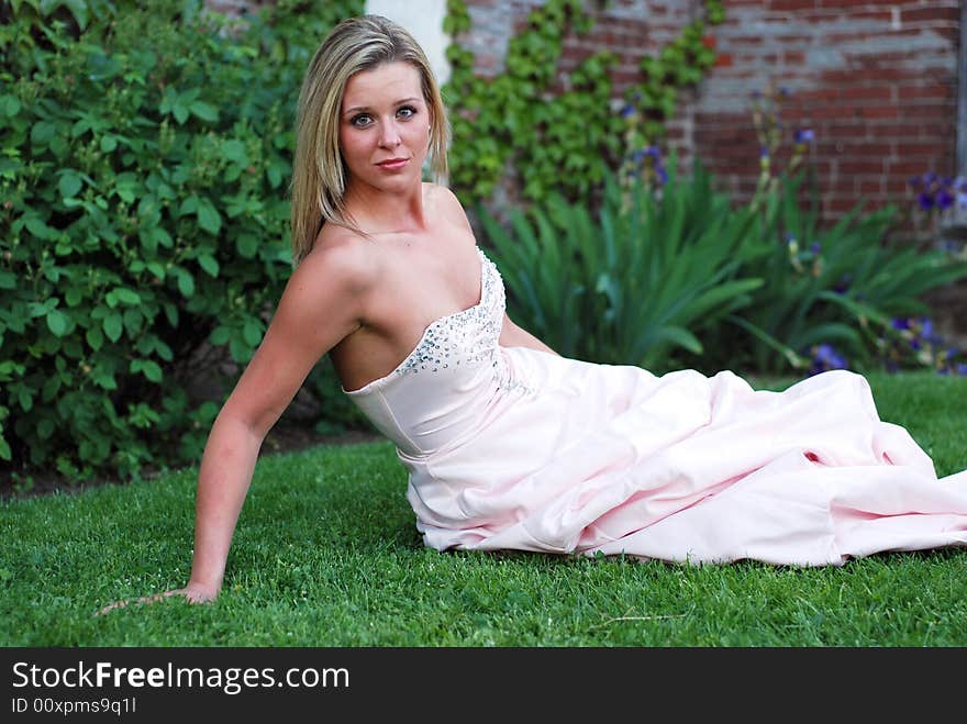 Attractive blond woman in a bridesmaid's dress sitting on a lush green lawn propping herself up with her arm. Attractive blond woman in a bridesmaid's dress sitting on a lush green lawn propping herself up with her arm.