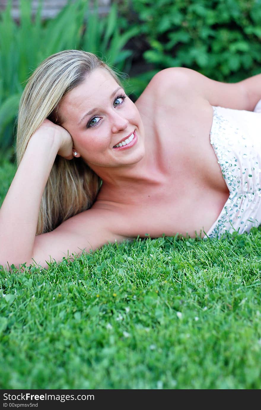 Attractive blond woman in a bridesmaid's dress lying on a lush green lawn propping her head up on her hand. Vertically framed shot. Attractive blond woman in a bridesmaid's dress lying on a lush green lawn propping her head up on her hand. Vertically framed shot.