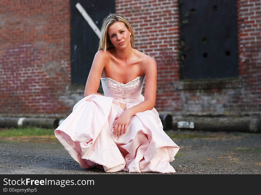 Horizontally framed outdoor shot of an attractive bridesmaid crouching down in front of red brick wall. Horizontally framed outdoor shot of an attractive bridesmaid crouching down in front of red brick wall.