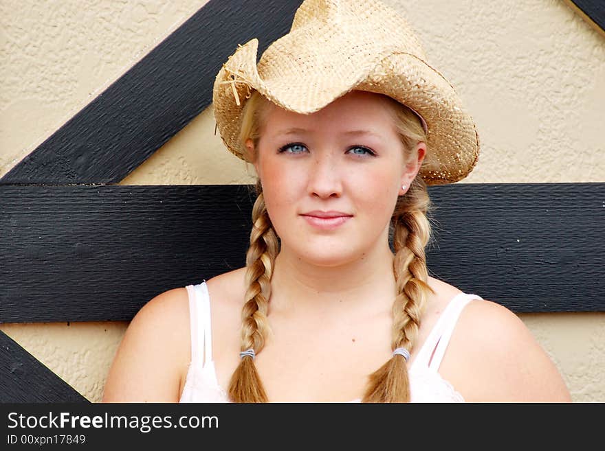 Horizontally framed outdoor shot of a smiling teenage girl, with blond hair and blue eyes, standing next to barn door wearing a straw cowboy hat. Horizontally framed outdoor shot of a smiling teenage girl, with blond hair and blue eyes, standing next to barn door wearing a straw cowboy hat.