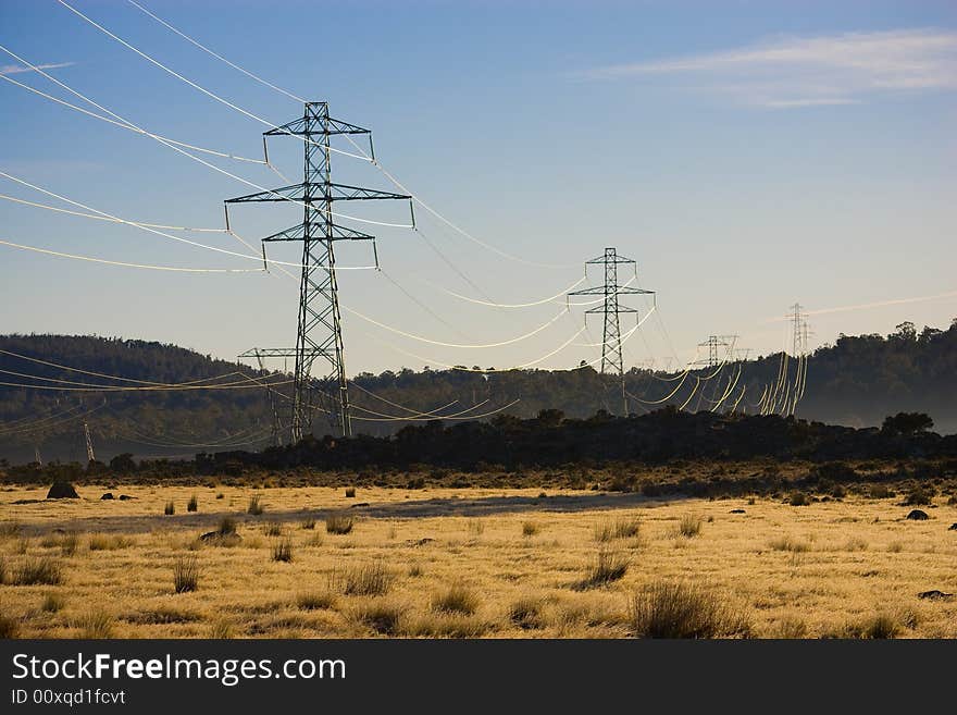 Power pylons and powerlines crossing farmland with dry grass in the forground