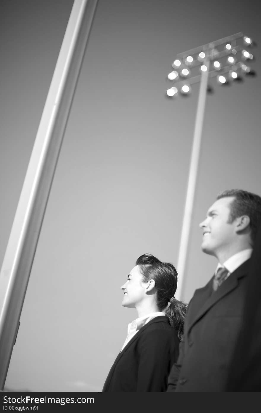 Profile view of businessman and businesswoman standing in formal wear in front of large lights. Profile view of businessman and businesswoman standing in formal wear in front of large lights