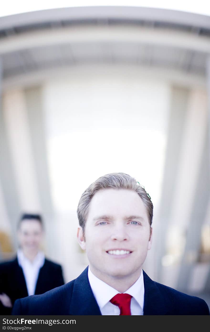 Attractive young businessman with businesswoman in background standing in front of building. Attractive young businessman with businesswoman in background standing in front of building