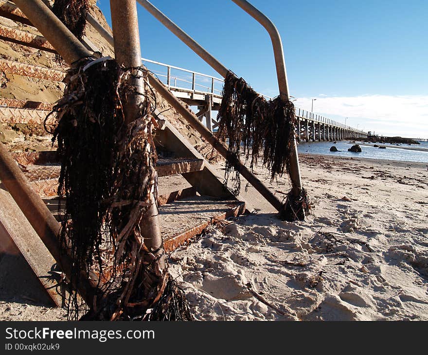 A rusty old staircase going down to the beach with a jetty and the ocean in the background. A rusty old staircase going down to the beach with a jetty and the ocean in the background.