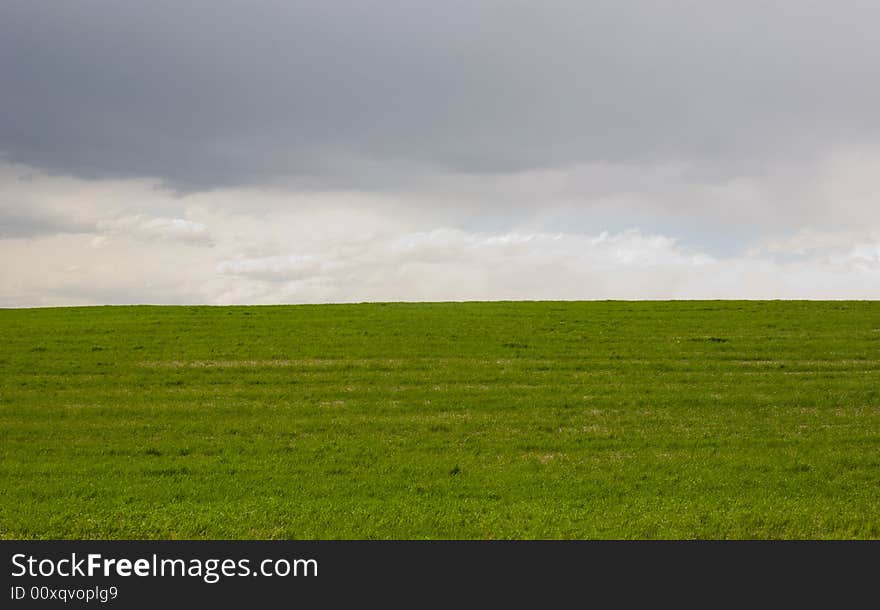 Green fields, the grey sky and white clouds. Green fields, the grey sky and white clouds