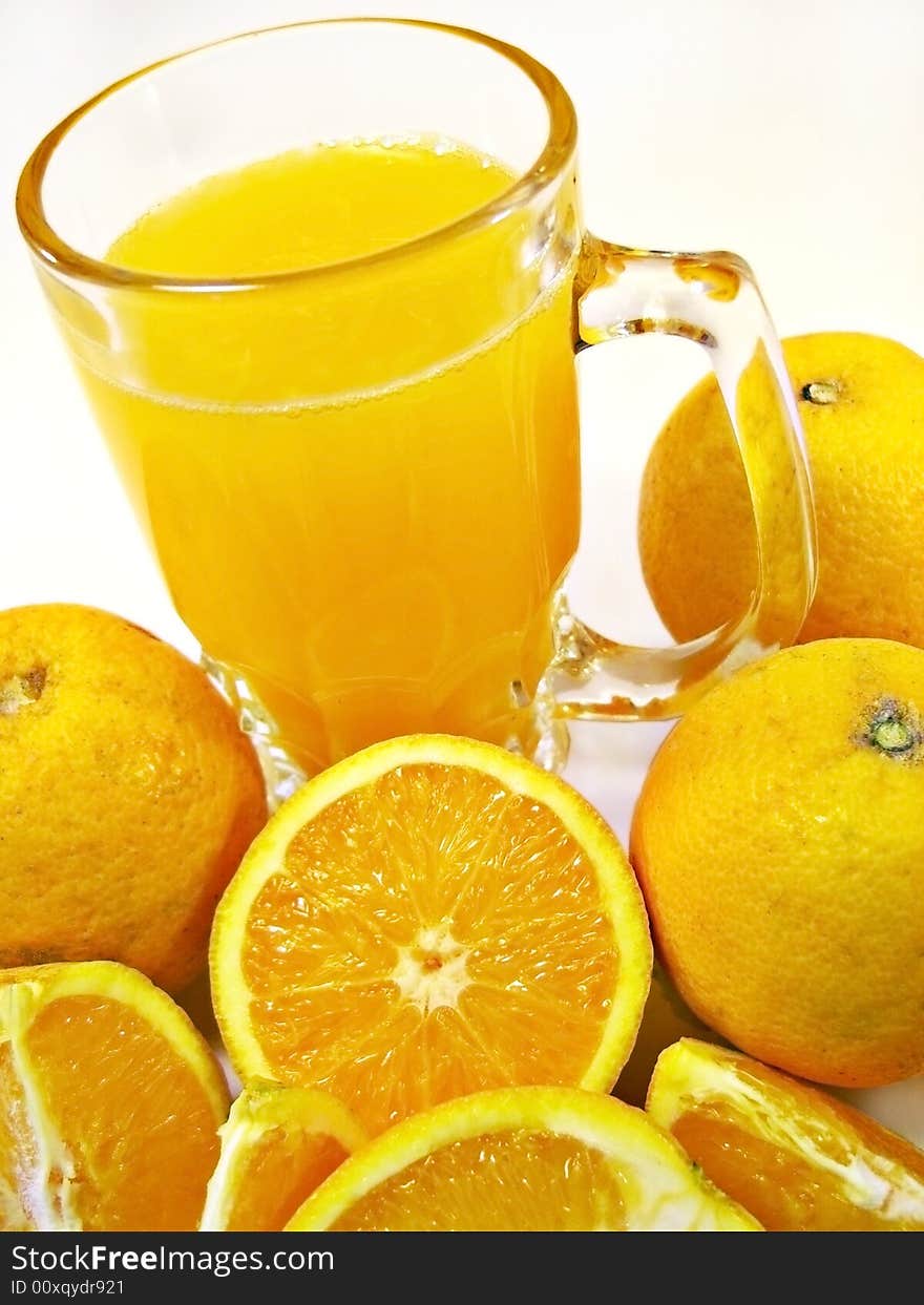 Glass of orange juice with some oranges surrounding it isolated on a white background.