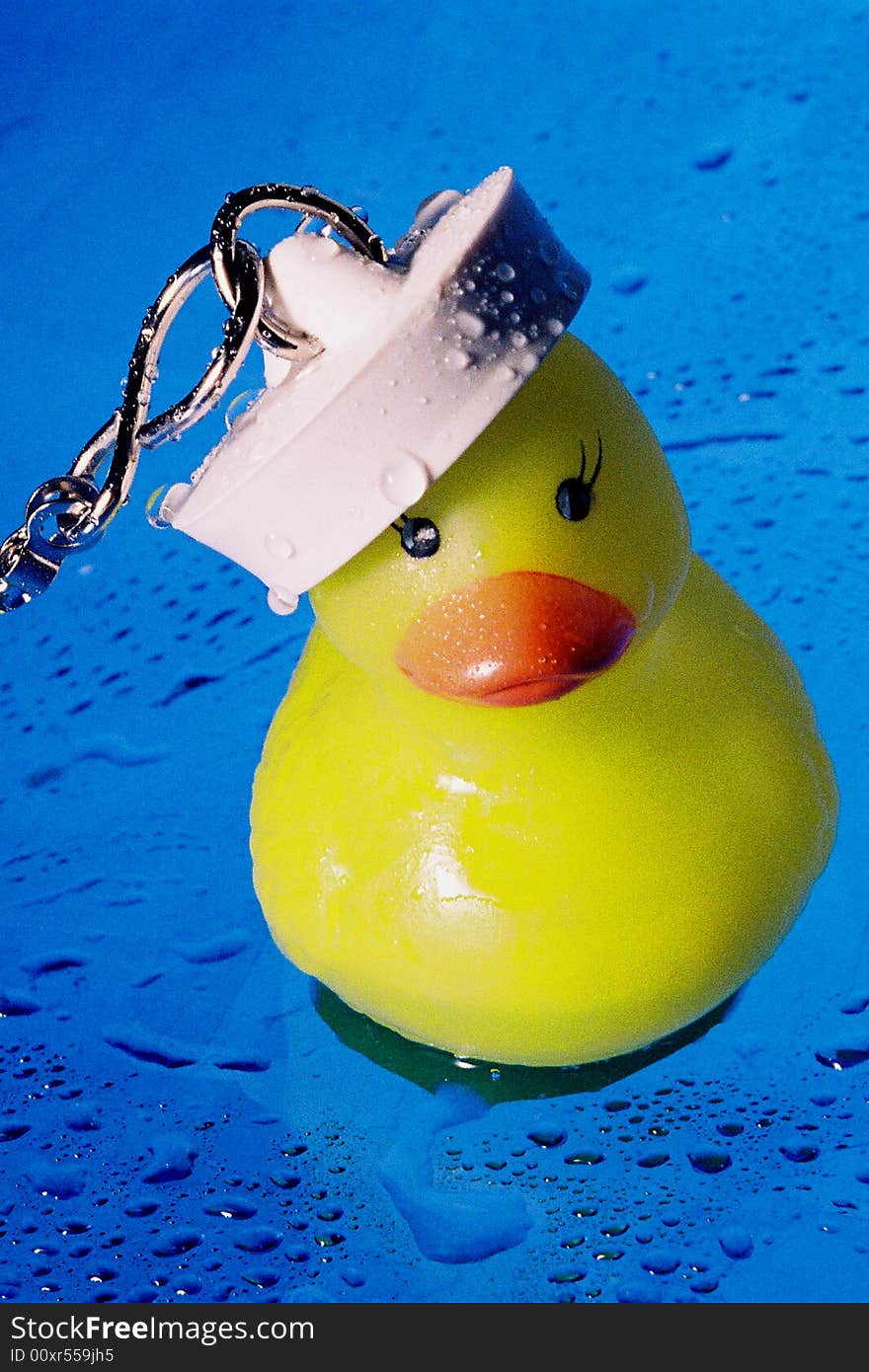 A colourful image of a rubber duck with a bath plug on his head that makes him look like a sailor ducky. the background is blue and is covered with little droplets