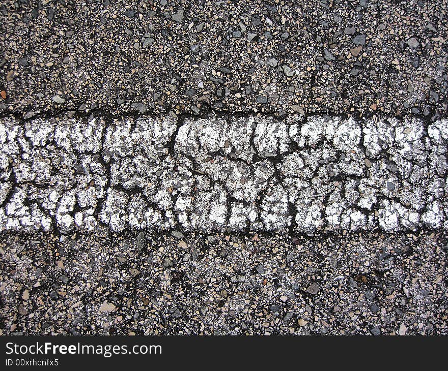 Straight white line view of an asphalt road with many cracks.