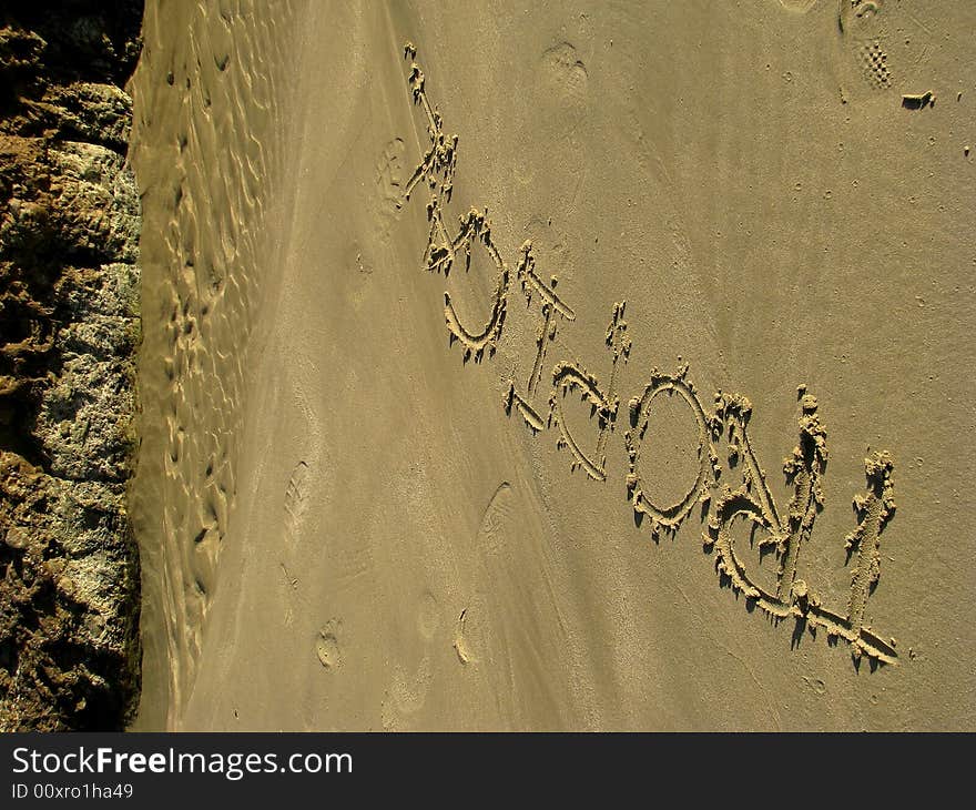 Tropical written in the sand with a finger and a rock pool in the back round. Tropical written in the sand with a finger and a rock pool in the back round