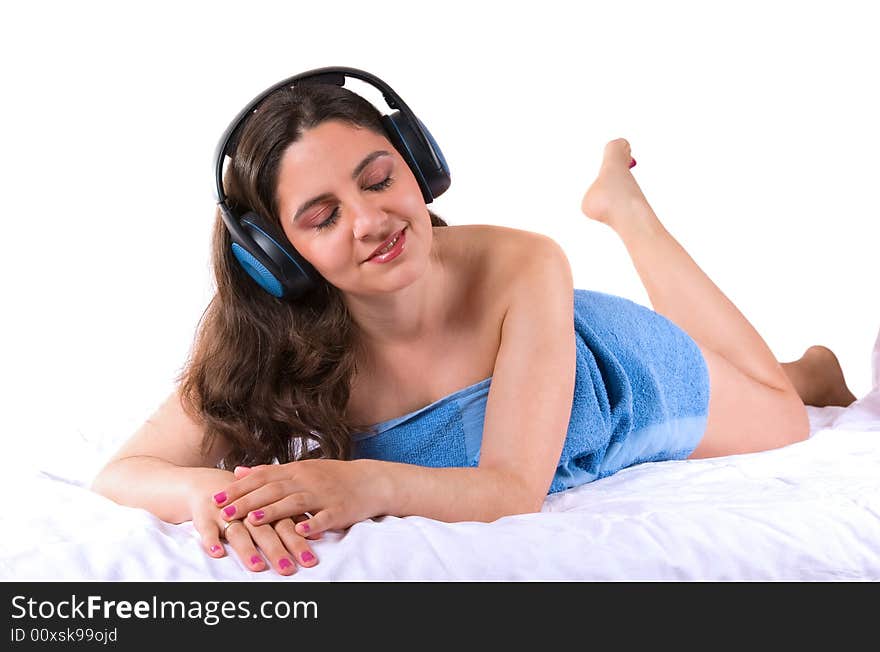 A beautiful girl, lying wrapped in a blue towel, wearing headphones, enjoying the music, with her eyes closed. A beautiful girl, lying wrapped in a blue towel, wearing headphones, enjoying the music, with her eyes closed