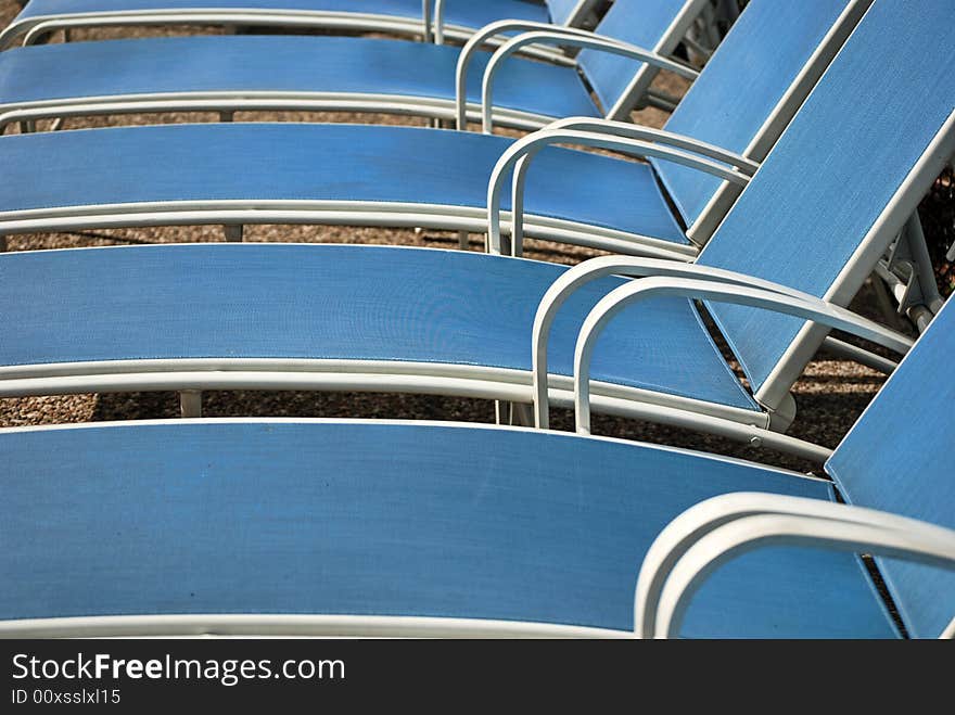 Row of blue chaise lounges by a pool.