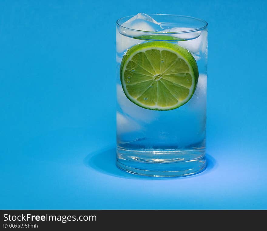 Glass of lime drink with ice cubes on blue background. Glass of lime drink with ice cubes on blue background.