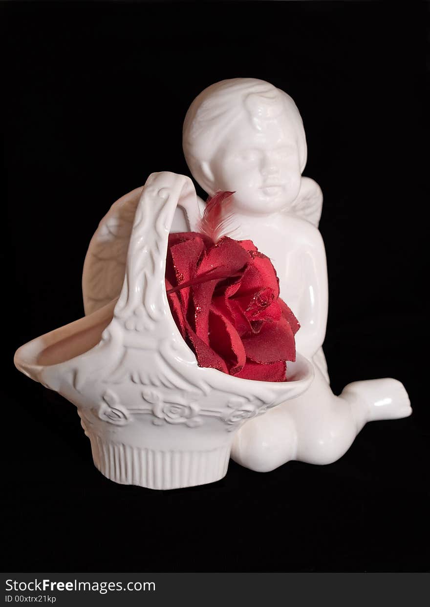 Love gift with ceramic angel figure and red artificial rose isolated on black. Love gift with ceramic angel figure and red artificial rose isolated on black