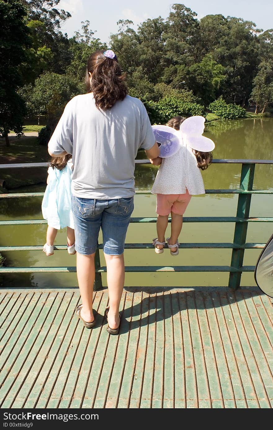 Mother and her two daughters looking over the railing of a bridge on a sunny day. Vertically framed shot. Mother and her two daughters looking over the railing of a bridge on a sunny day. Vertically framed shot.