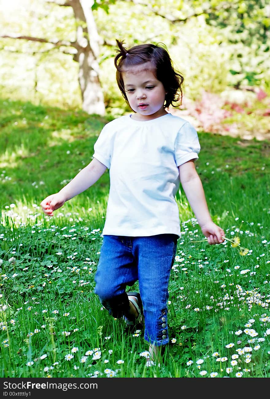 Cute little girl picking summer flowers on a sunny day in the park. Vertically framed shot.