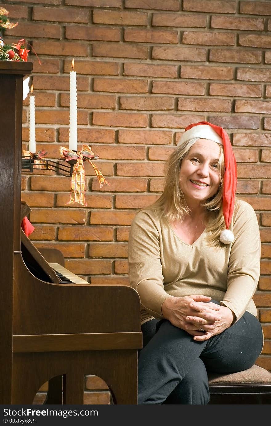 Senior woman sitting at an upright piano wearing a santa hat and smiling at the camera. Vertically framed shot. Senior woman sitting at an upright piano wearing a santa hat and smiling at the camera. Vertically framed shot.