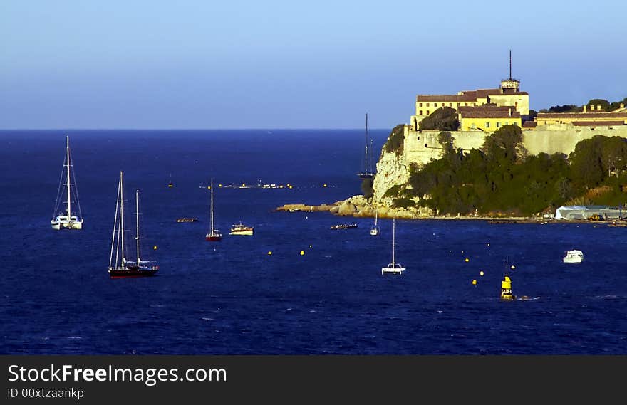 Sail boats float lazily off the coast of a picturesque island in France. Sail boats float lazily off the coast of a picturesque island in France