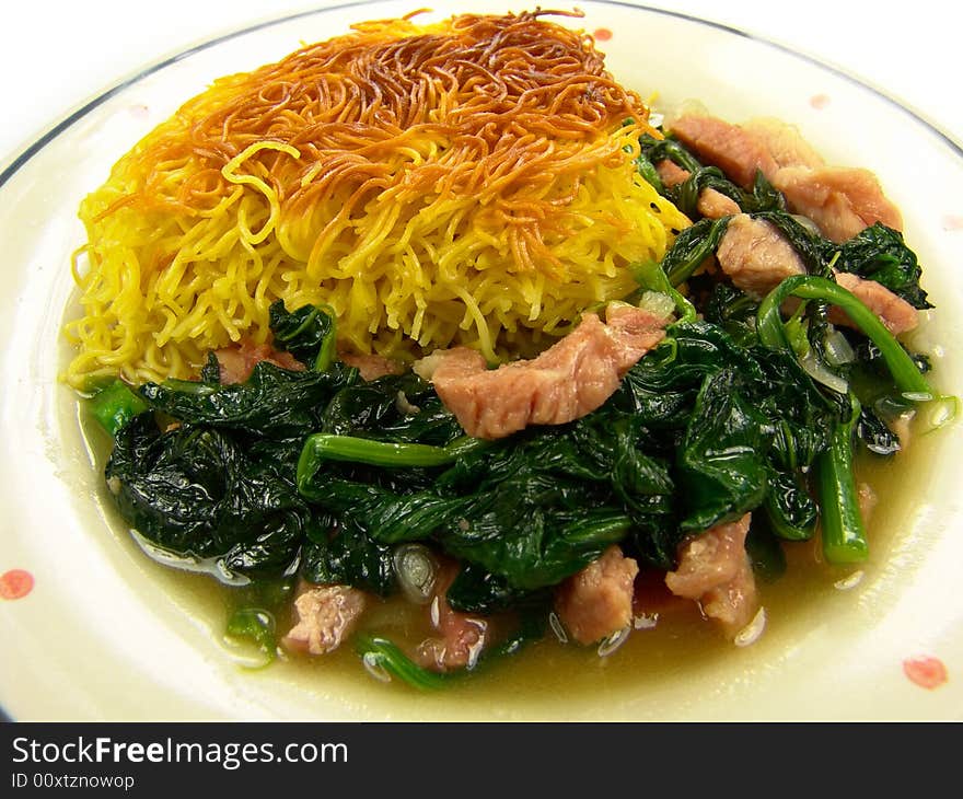 Closeup of a dish of Chinese fried noodles with green vegetable and ham on a ceramic plate. Closeup of a dish of Chinese fried noodles with green vegetable and ham on a ceramic plate