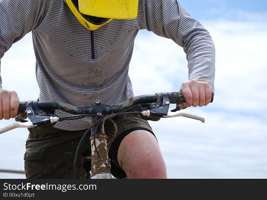 Mud-splattered mountain biker against a dirt road and green pasture. Mud-splattered mountain biker against a dirt road and green pasture.