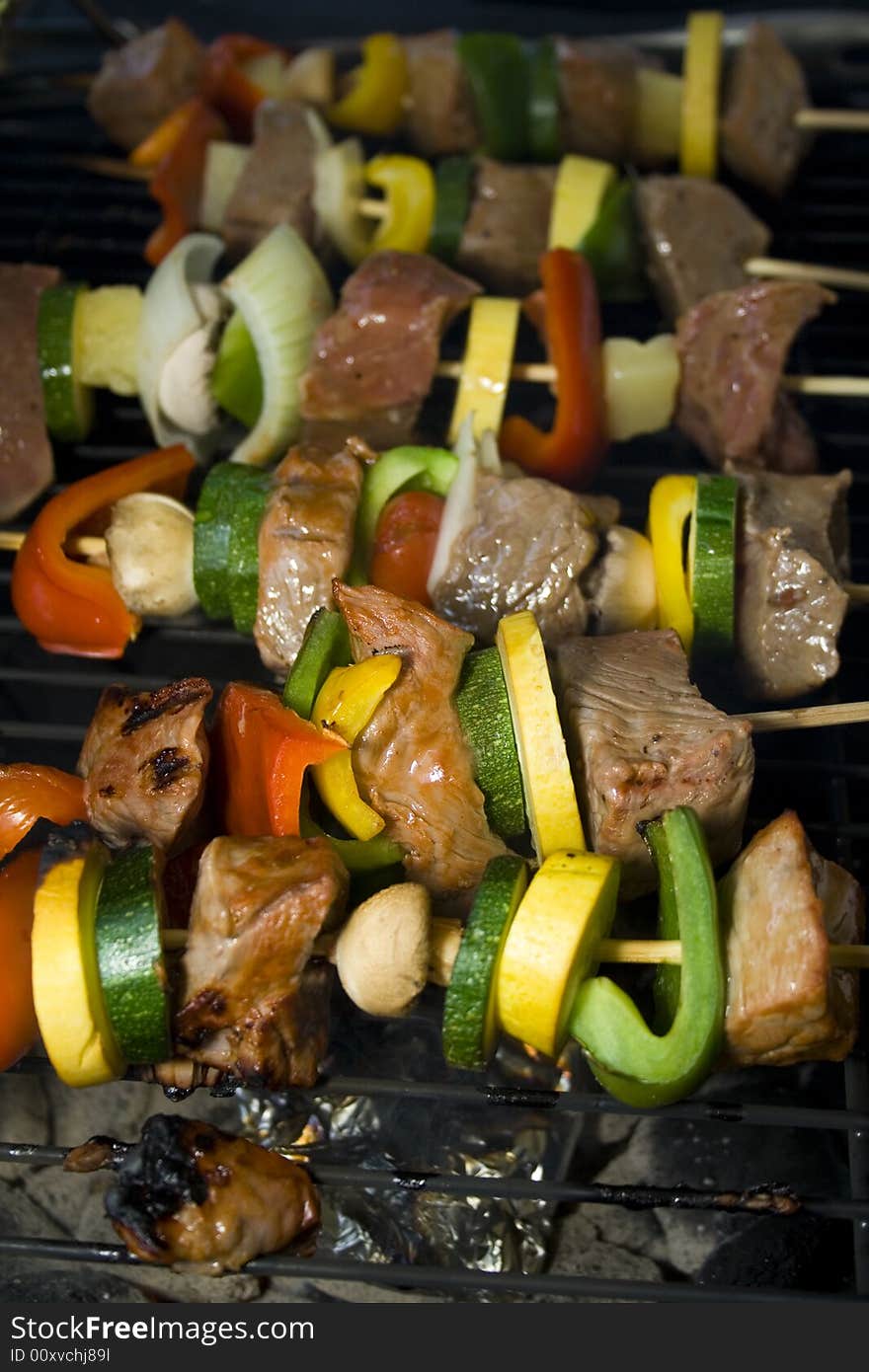 Several Shishkabobs lined up  cooking on a grill