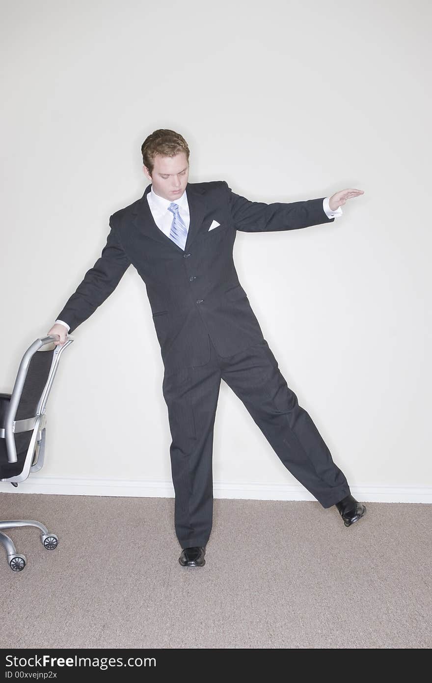 Businessman wearing a dark suit uses balance to keep himself steady while holding on to a business chair. Businessman wearing a dark suit uses balance to keep himself steady while holding on to a business chair