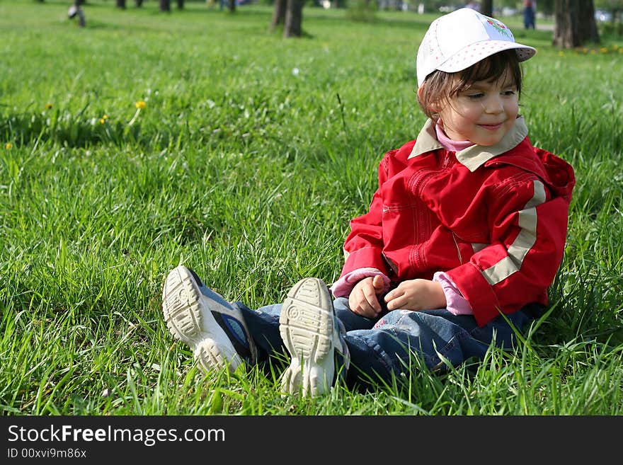 Little girl in the park sitting on green grass