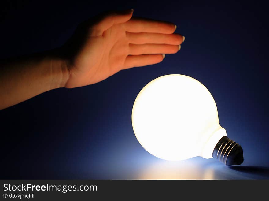 One glowing light bulb and female hand on a blue background. One glowing light bulb and female hand on a blue background.