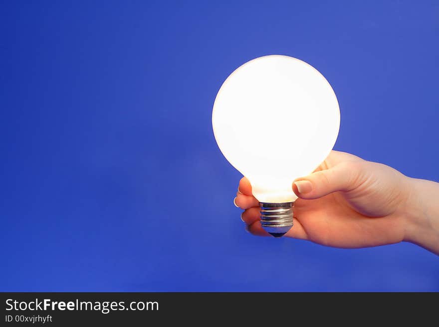 Female hand holding glowing light bulb on a blue background.