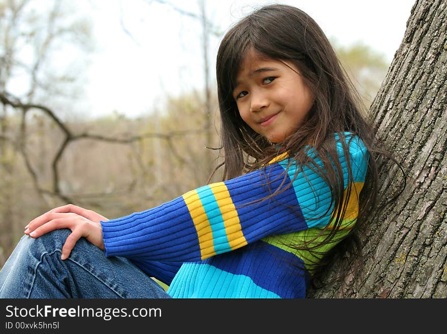 Adorable little girl sitting against  tree