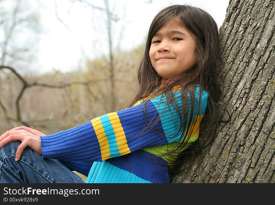 Adorable little girl sitting against  tree