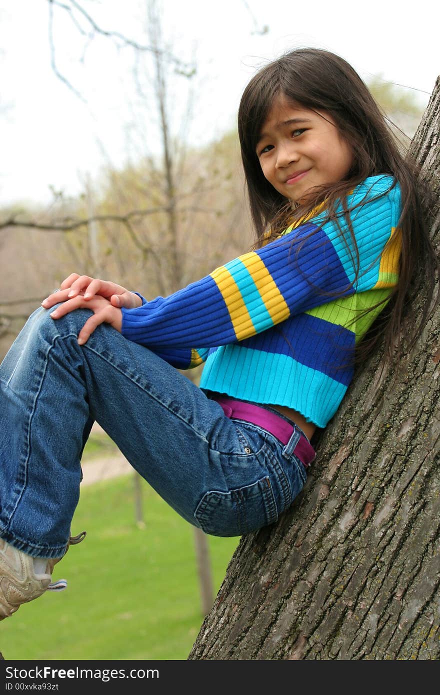 Adorable little girl sitting against  tree