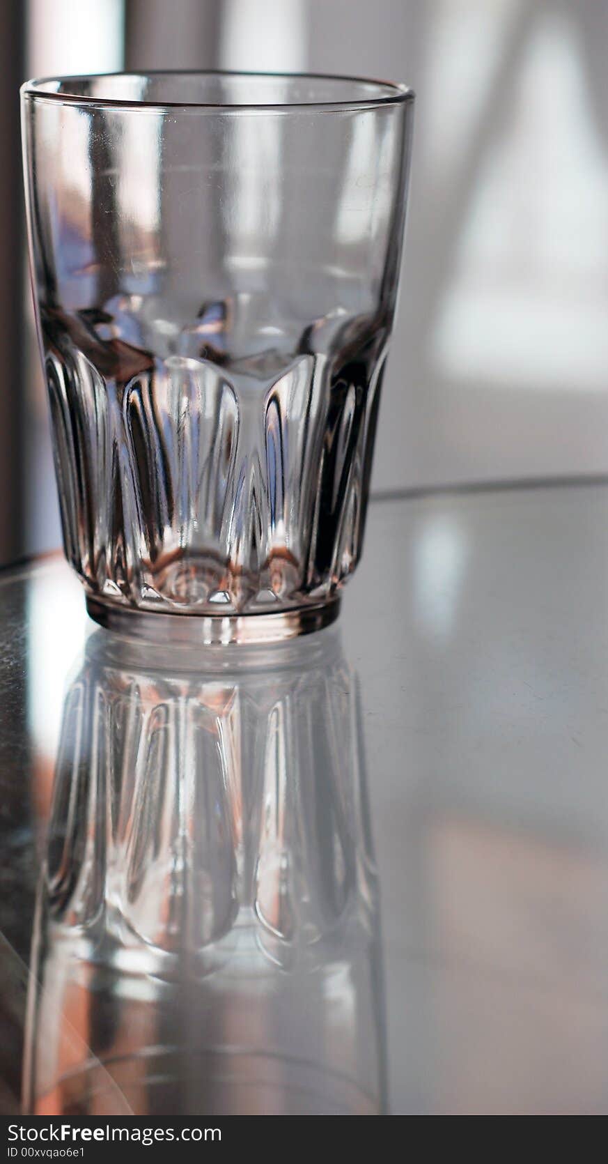 An empty glass sits with it's reflection on a glass table. An empty glass sits with it's reflection on a glass table.