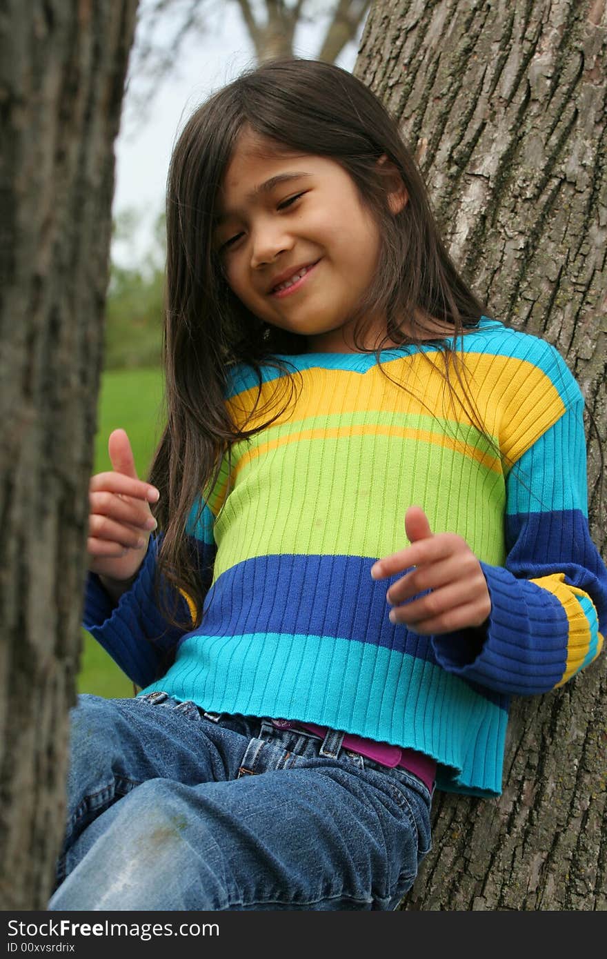 Adorable little girl sitting up against tree