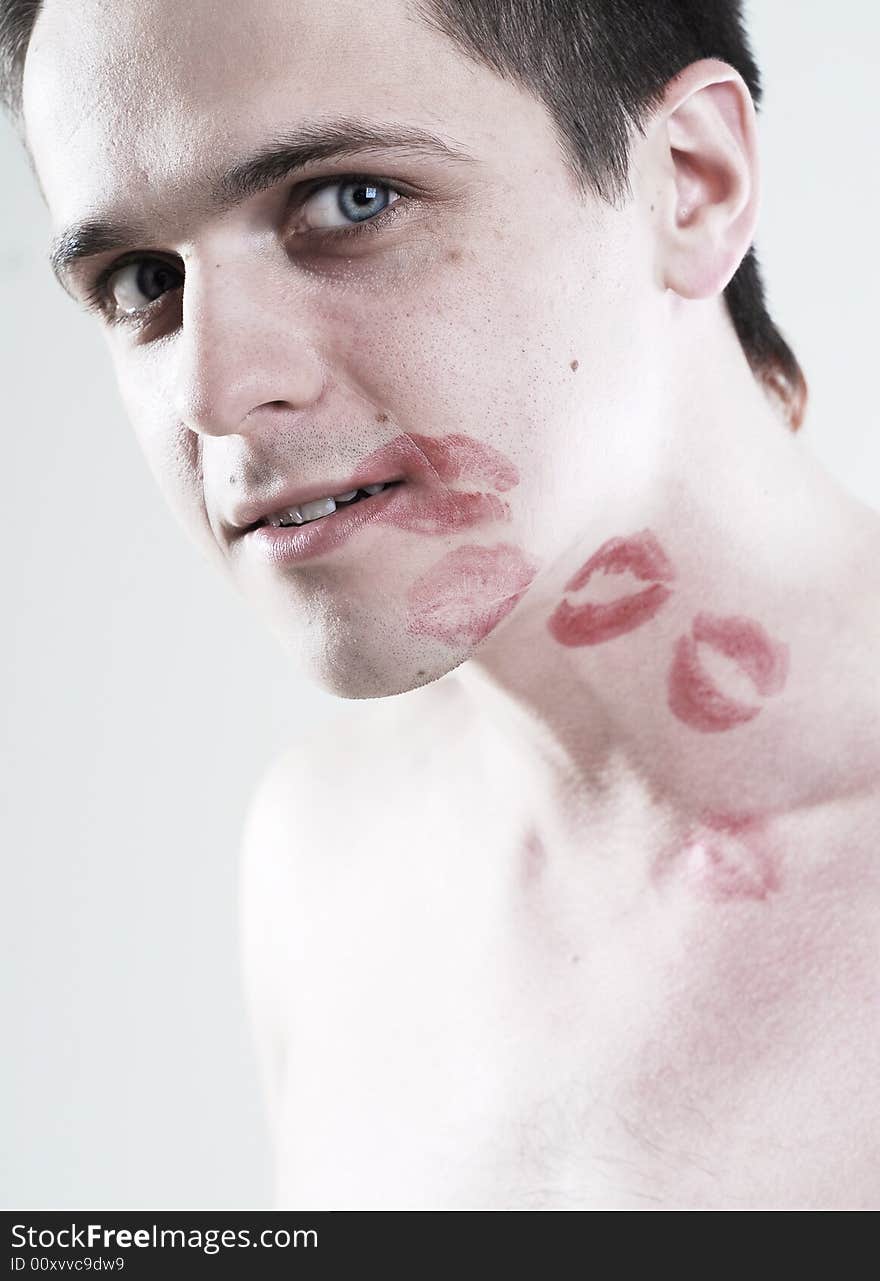 Red kisses on face of young man at white background