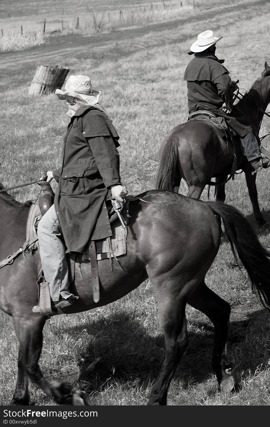 Black and white portrait of a menacing trio of masked bandits on horseback