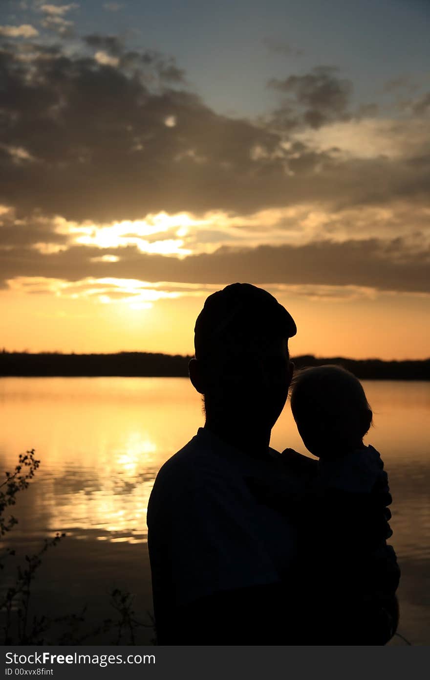 Silhouette portrait of a Father holding his young Daughter on the shore of a lake at sunset. Silhouette portrait of a Father holding his young Daughter on the shore of a lake at sunset