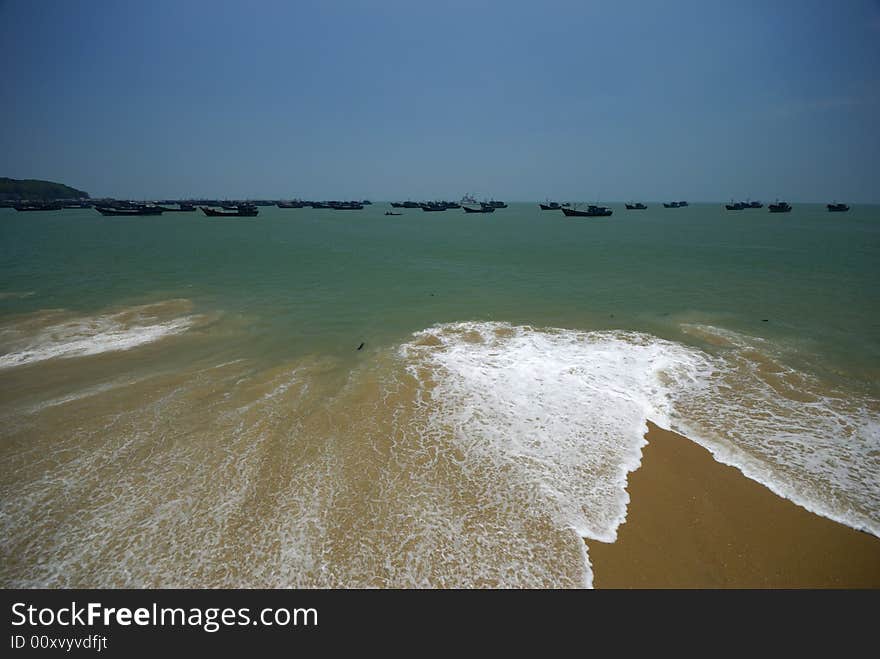 Sea beach against clear blue sky.Some ships in distance.