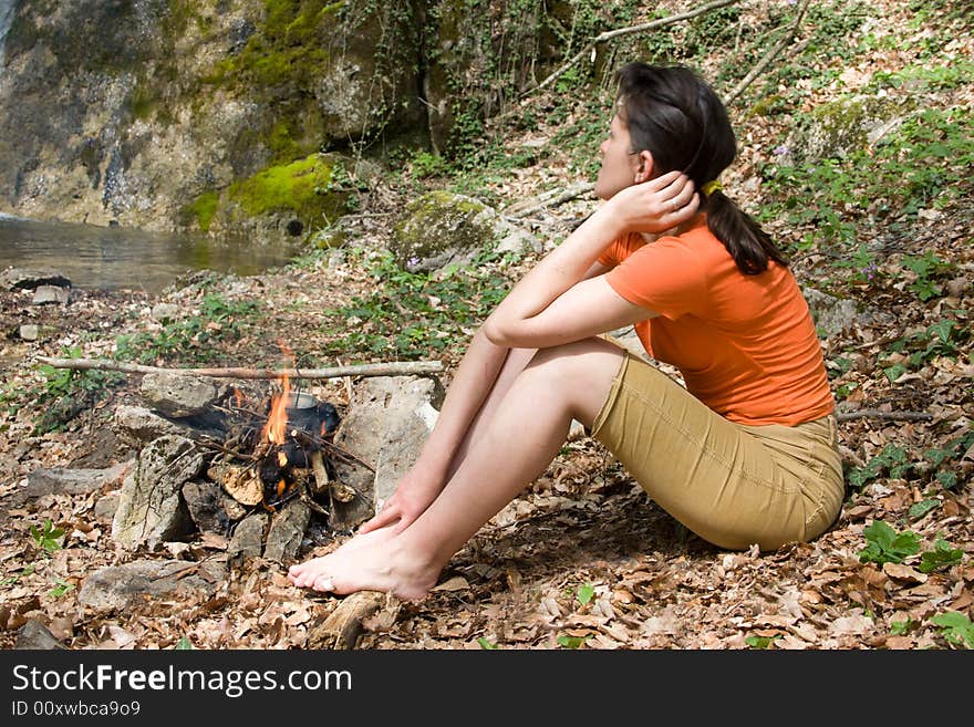 Girl sitting near of fire on the river bank