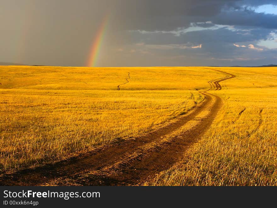 Road, yellow hills and rainbow.