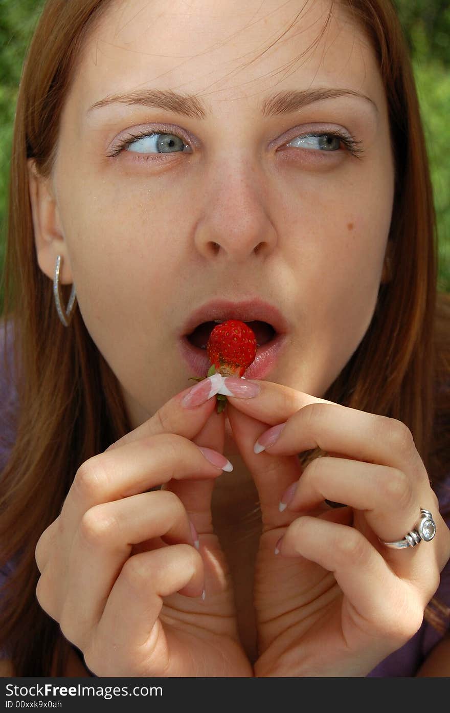 Beautiful young woman with nice long hair is eating a small strawberry. Beautiful young woman with nice long hair is eating a small strawberry.