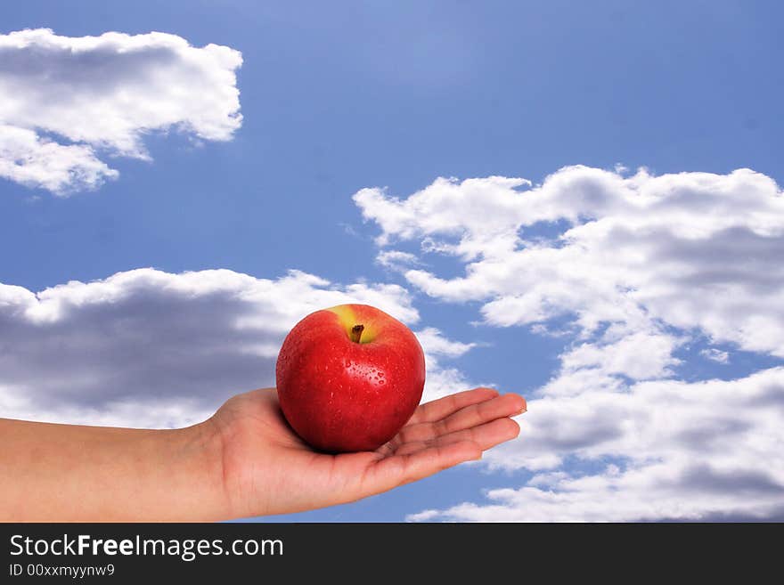 Apple in palm with sky background with beads of water on apple