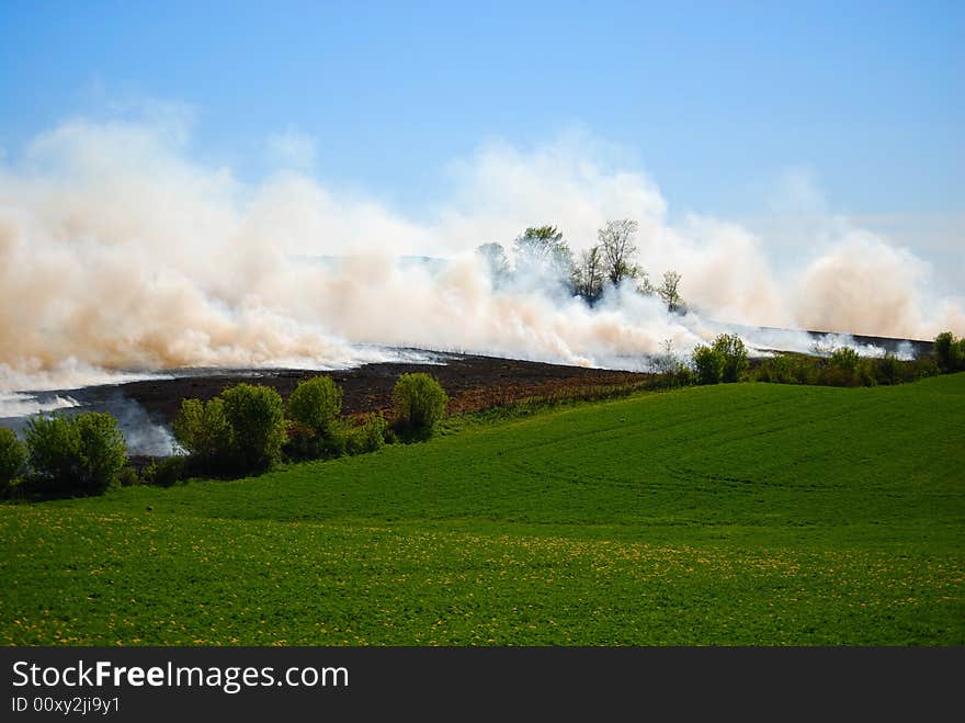 Farmland on fire with clouds of smoke and green pasture. Farmland on fire with clouds of smoke and green pasture