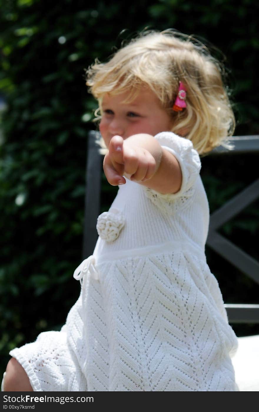 Little girl points at the viewer while sitting in a garden chair. Little girl points at the viewer while sitting in a garden chair.